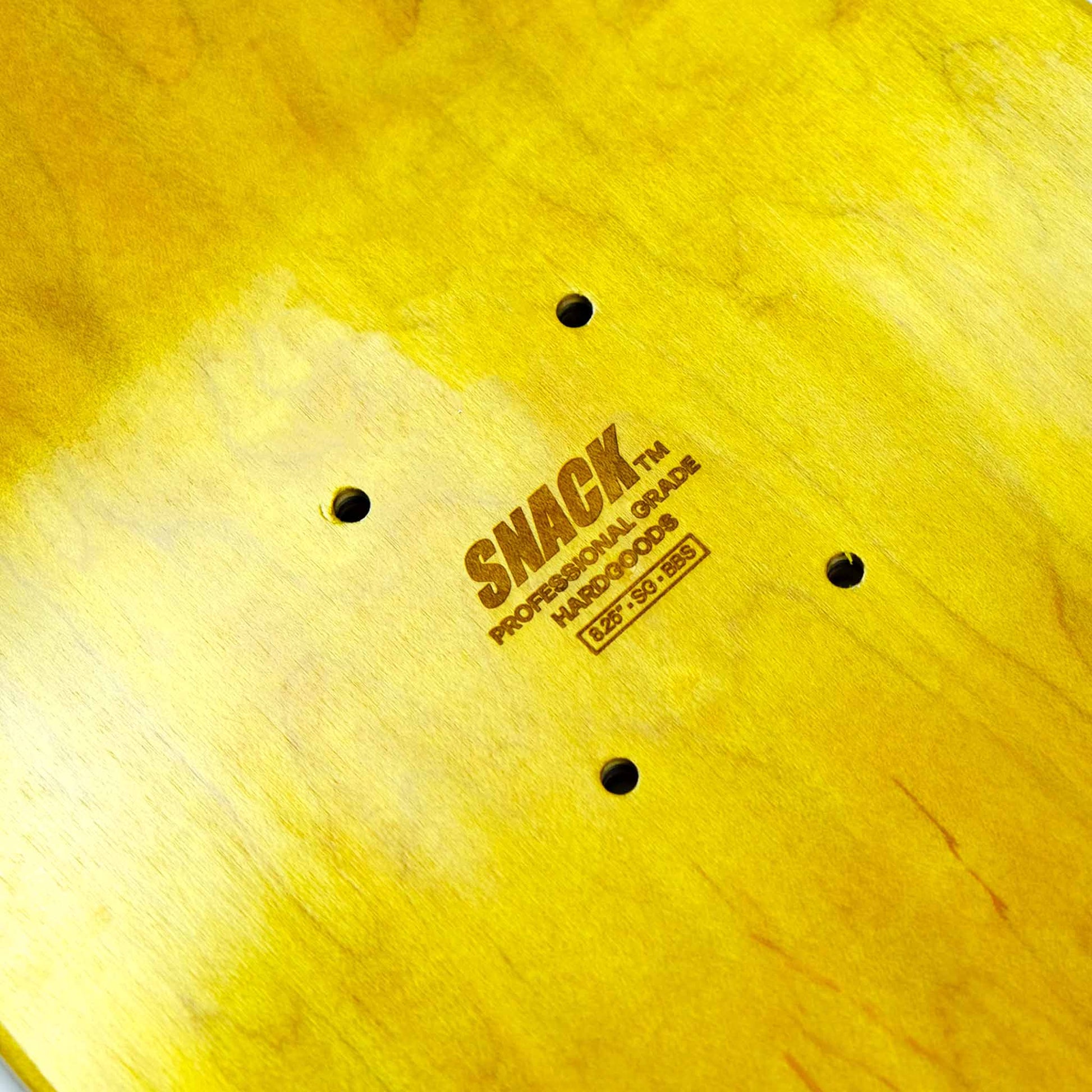 Close-up of a yellow skateboard deck with 'Snack' branding.
