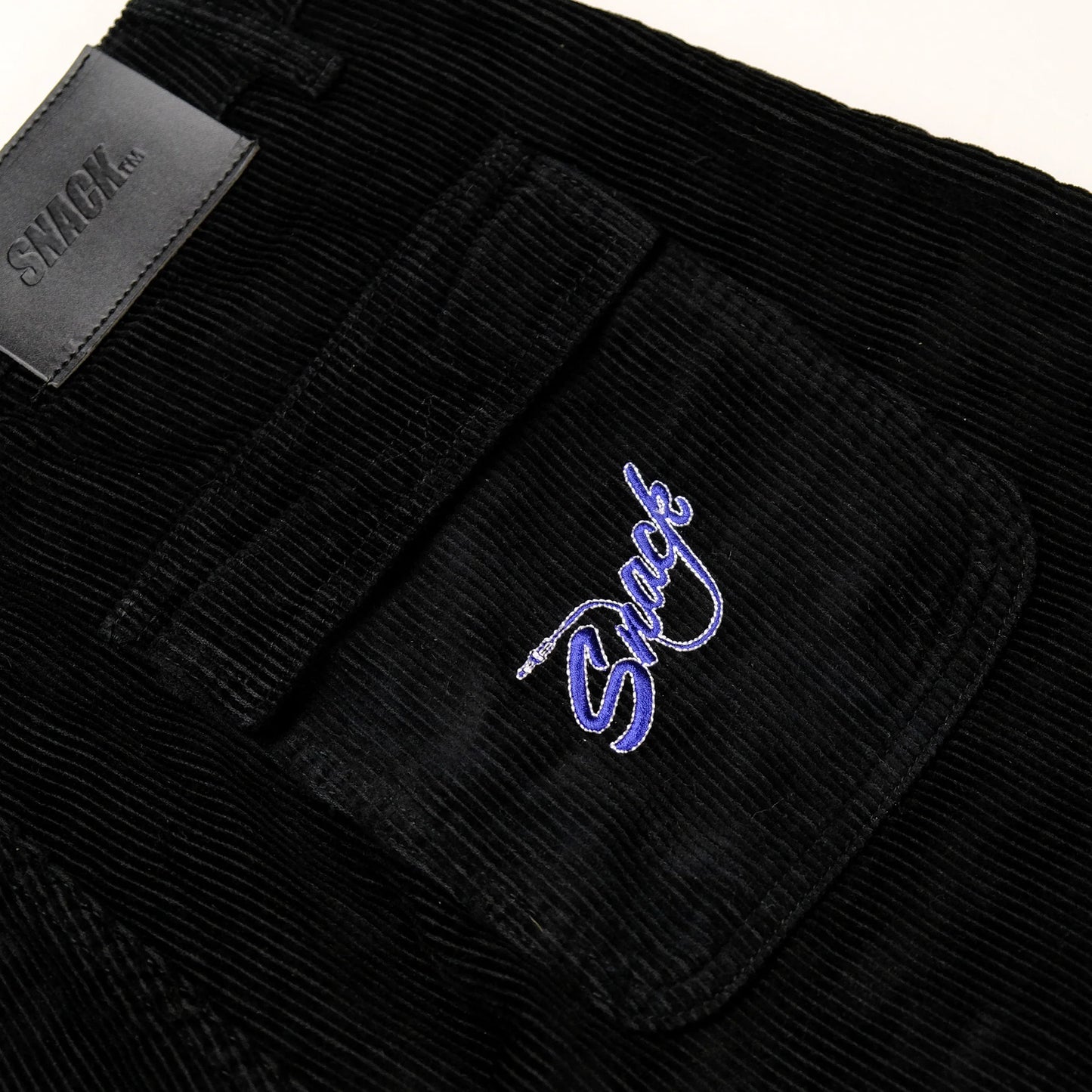 Black corduroy pants with a brand logo on the pocket against a white background