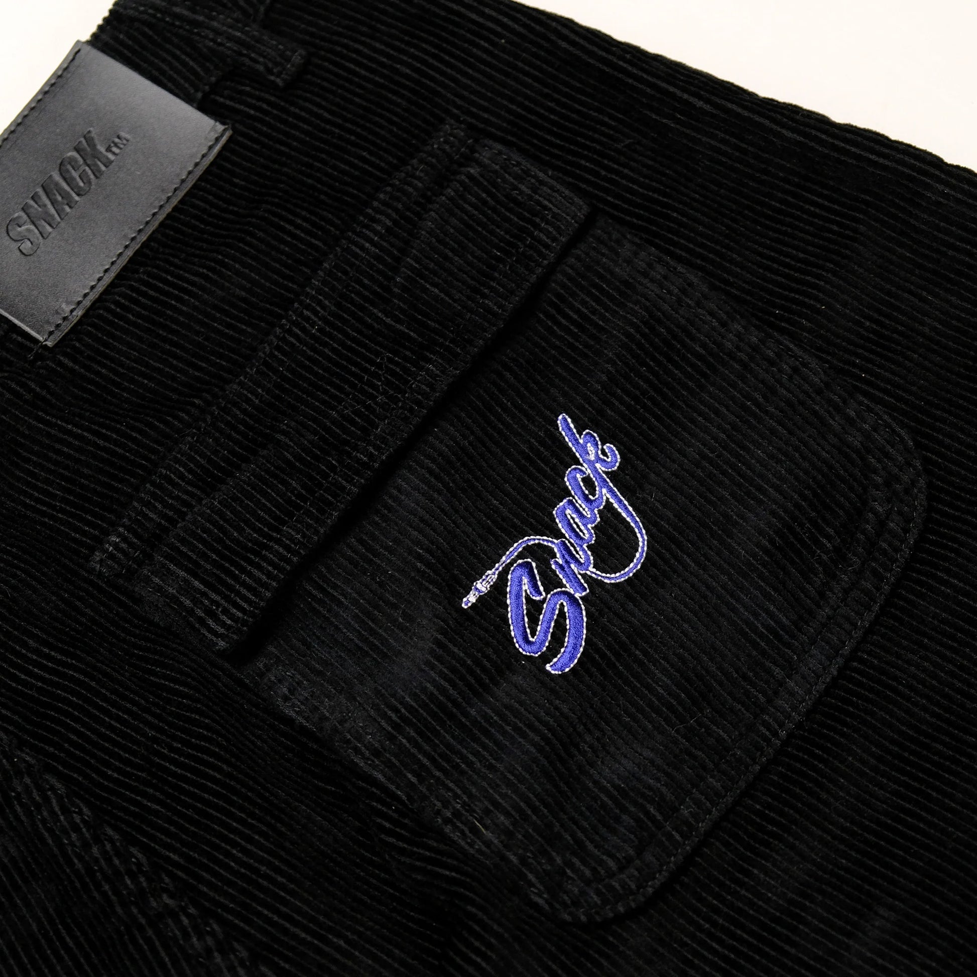 Black corduroy pants with a brand logo on the pocket against a white background