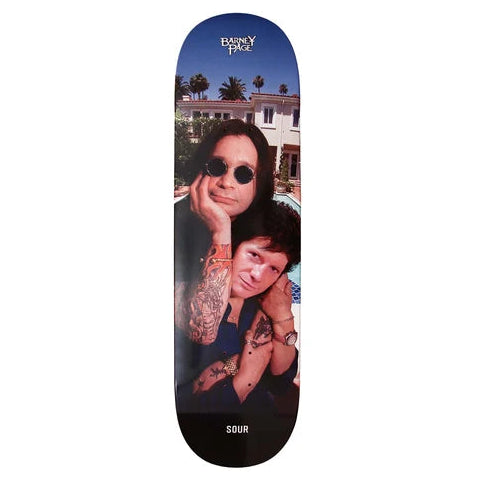 A skateboard deck featuring a printed graphic of two people, one with sunglasses, set against a blue sky and white building background, with the text  'SOUR' at the bottom.