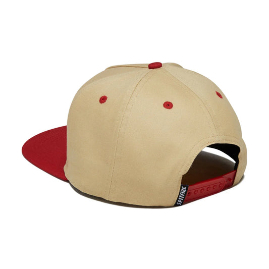 A structured snapback cap shown from a three-quarters rear angle, featuring a beige crown with red button and eyelet accents, and a contrasting red flat brim.