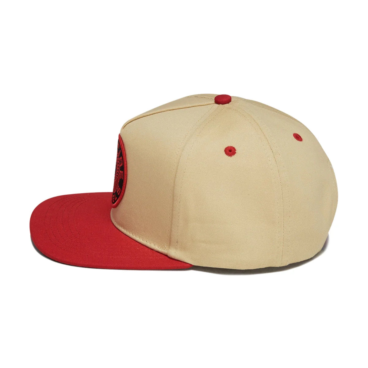 A structured baseball cap with a beige crown and a red flat brim, featuring a red button on top, red eyelets, and a red embroidered patch on the side.