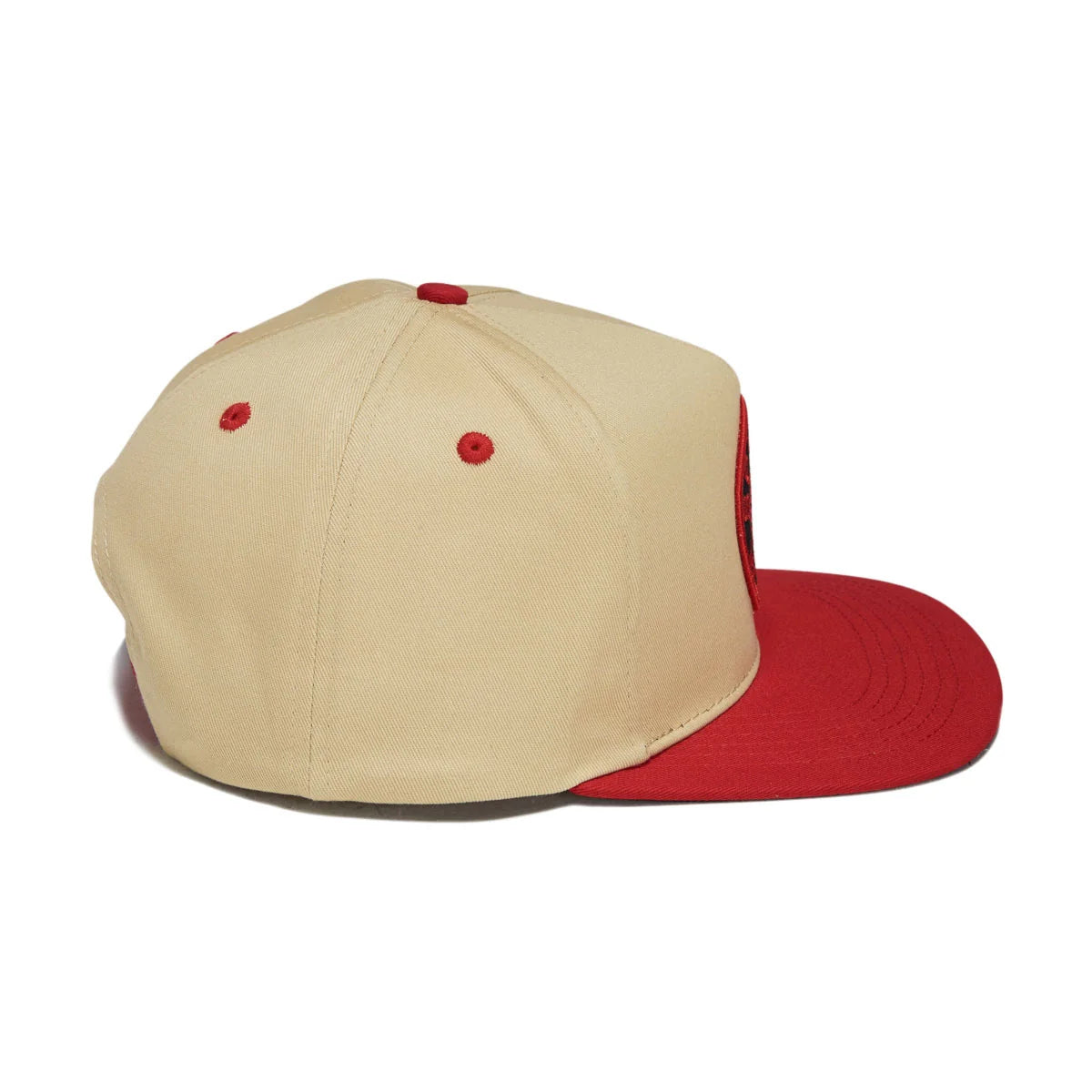 A structured baseball cap with a beige crown and a red flat brim, featuring red button eyelets and a red side logo patch.