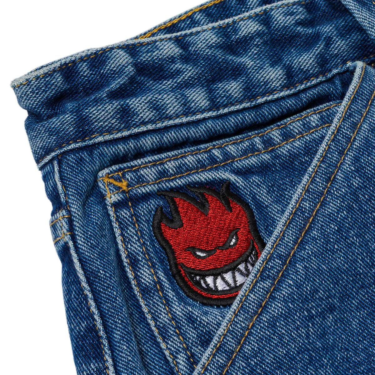 Close-up of blue denim fabric with a red and black embroidered patch featuring a angry face design.