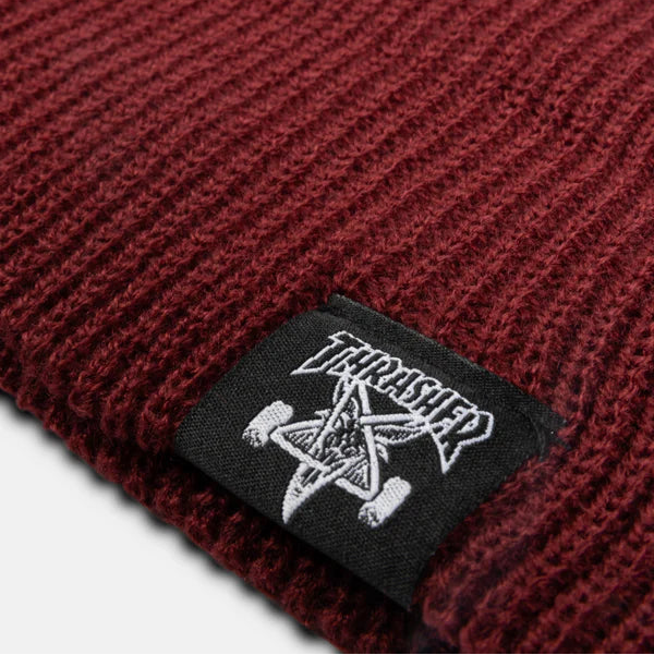 Close-up of a red knit beanie with a branded tag featuring a pentagram and skateboard design.