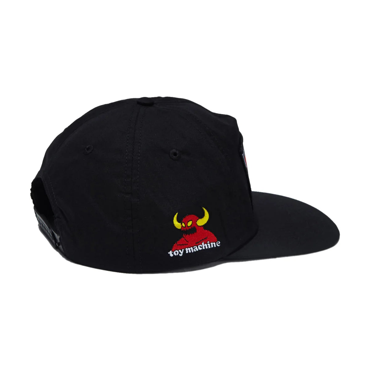 A black snapback cap featuring a small embroidered logo on the front panel with a red devil figure, yellow horns, and the text 'toy machine' in white, shown against a plain white background.