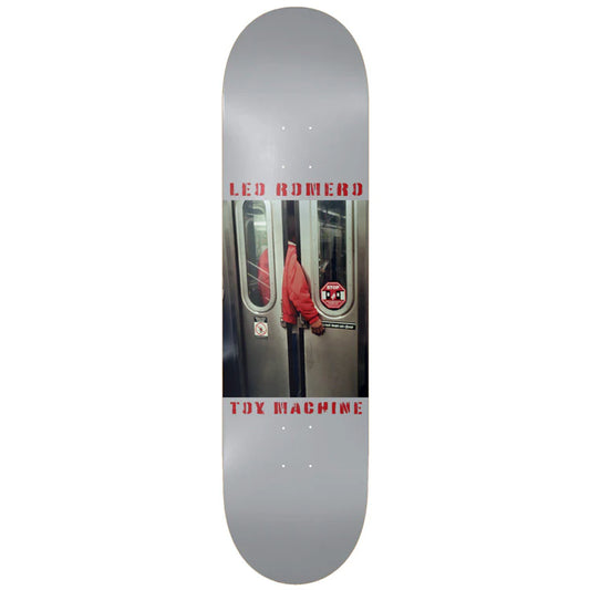 Skateboard deck with a graphic design featuring a person in a red jacket and 'Toy Machine' branding on a white background.