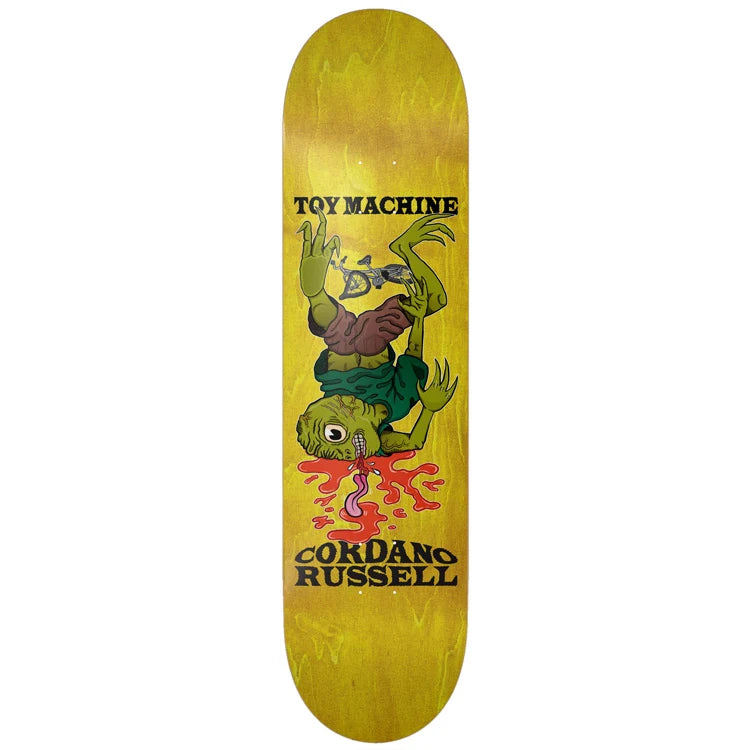 A skateboard deck featuring a yellow wood-grain finish with a graphic of a green alien-like character falling into red liquid, with the text 'TOY MACHINE' and 'CORDANO RUSSELL' printed in black.