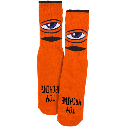 Orange socks with eye design and 'Toy Machine' text on a white background